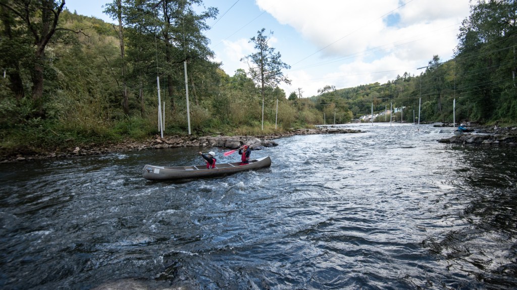 Two children canoeing on the rapids at Symonds Yat on the River Wye. The water is relatively calm. The children are laughing and whooping as they pass the busiest part of the river.