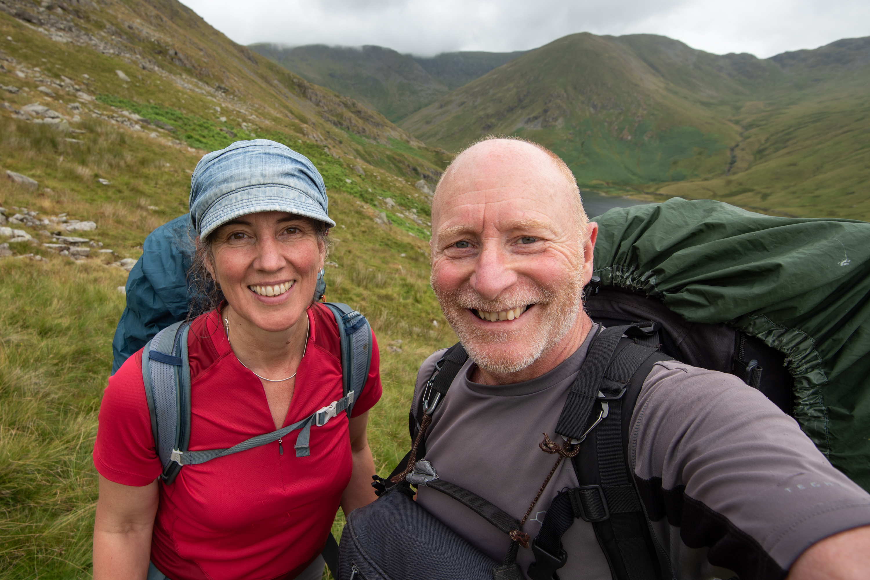 A woman and a man smile at the camera with hills in the background