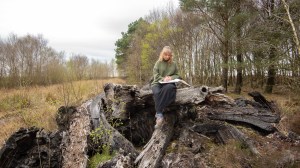 A woman sits on an old section of blackened bog oak, sketching in a book.