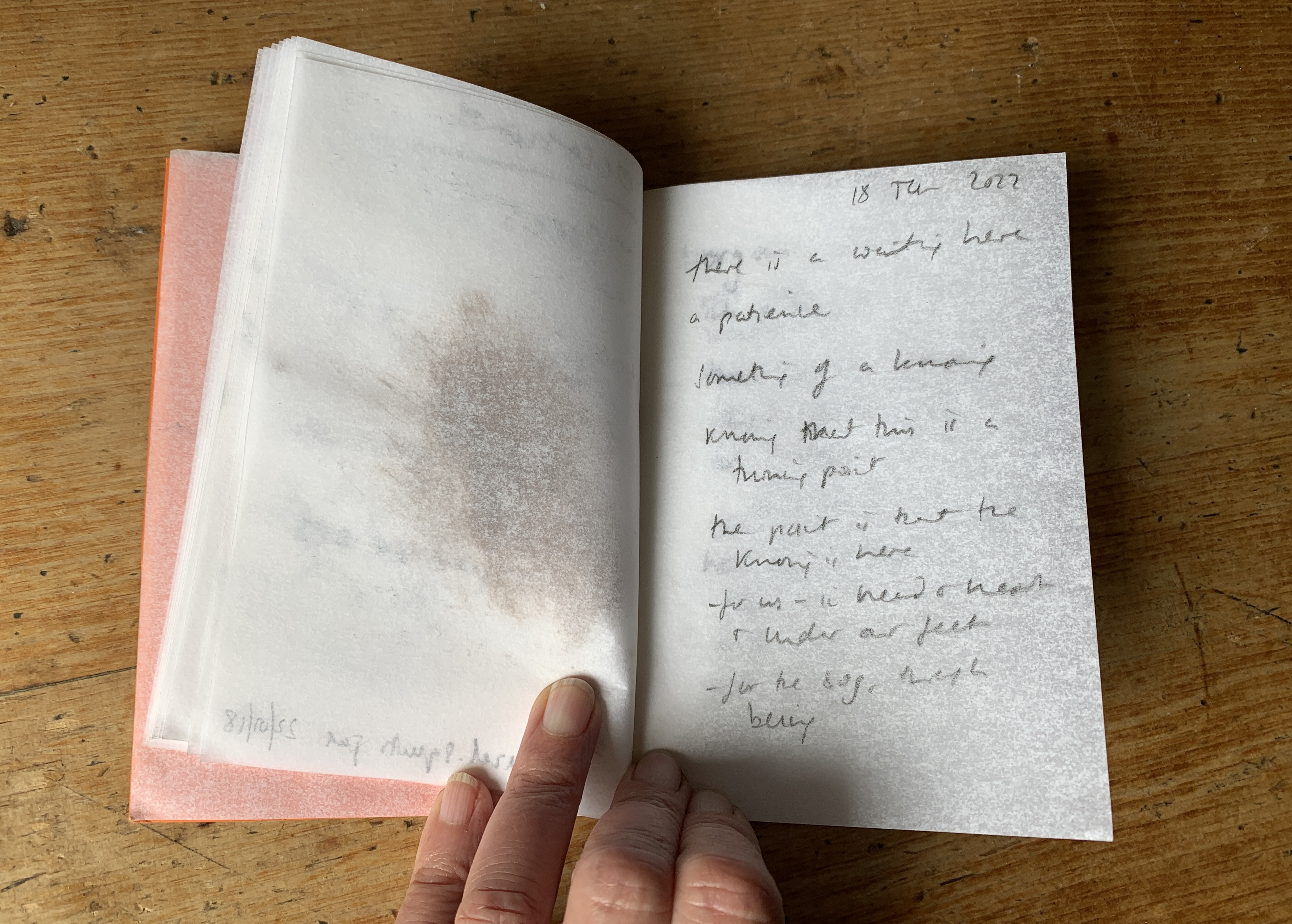 A notebook is held open on a table, showing pencil-writing; these are notes made by poet Harriet Fraser