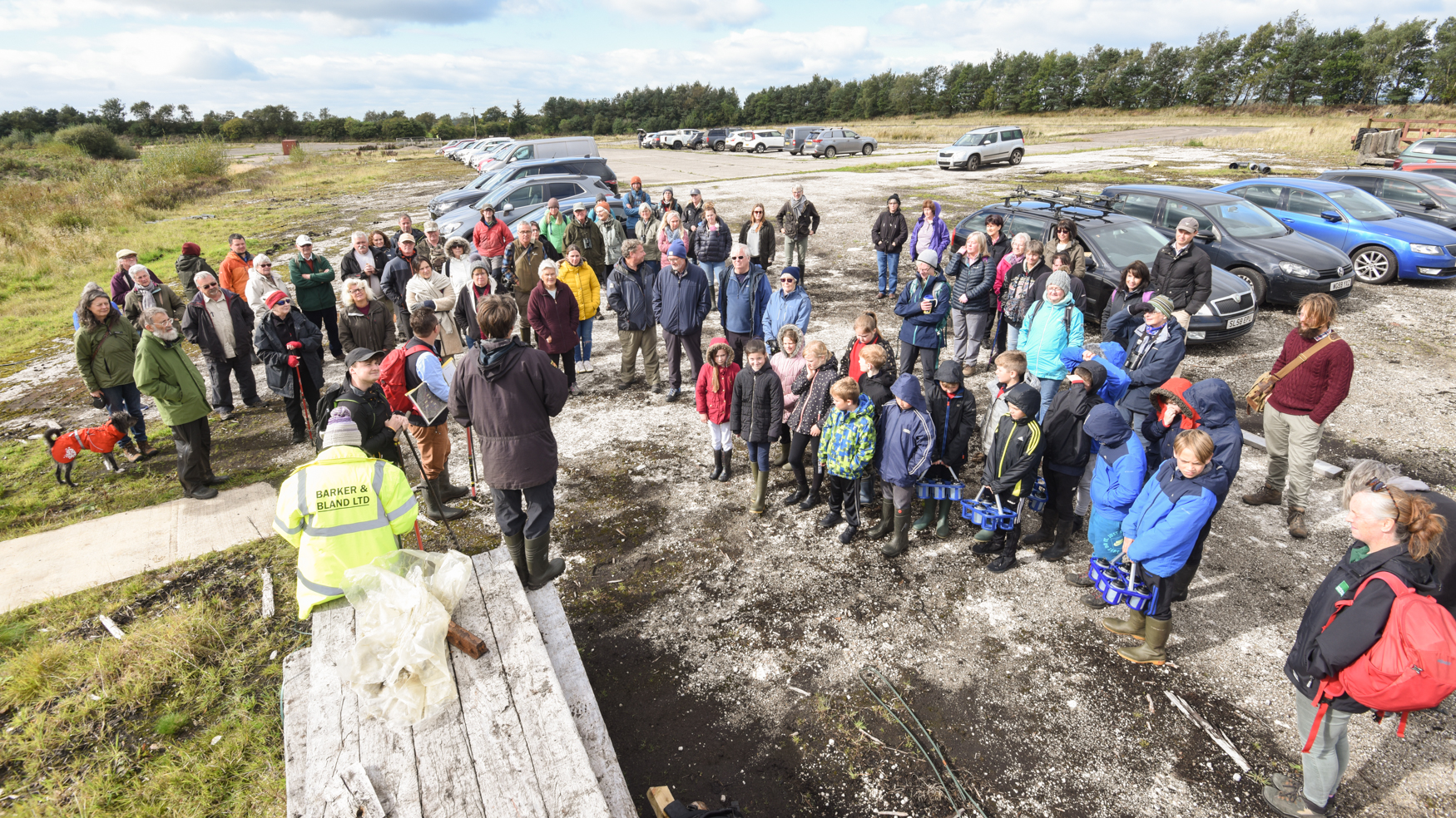 A group of people stand with cars in the background