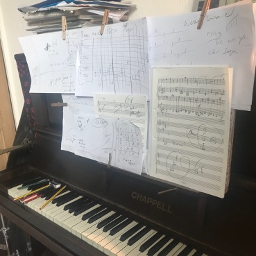 An image of a piano with sheets of paper and notations; Colin Riley's composition process