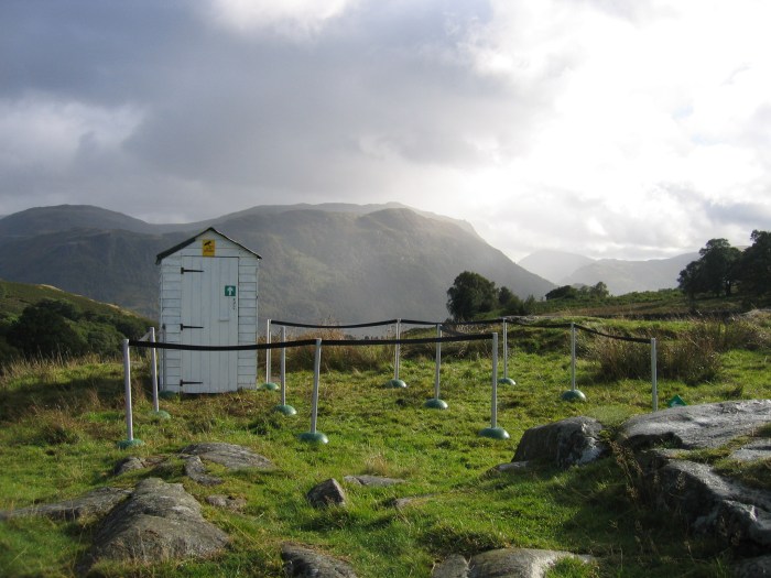 A white shed placed on a hillside, with a rope set out around it