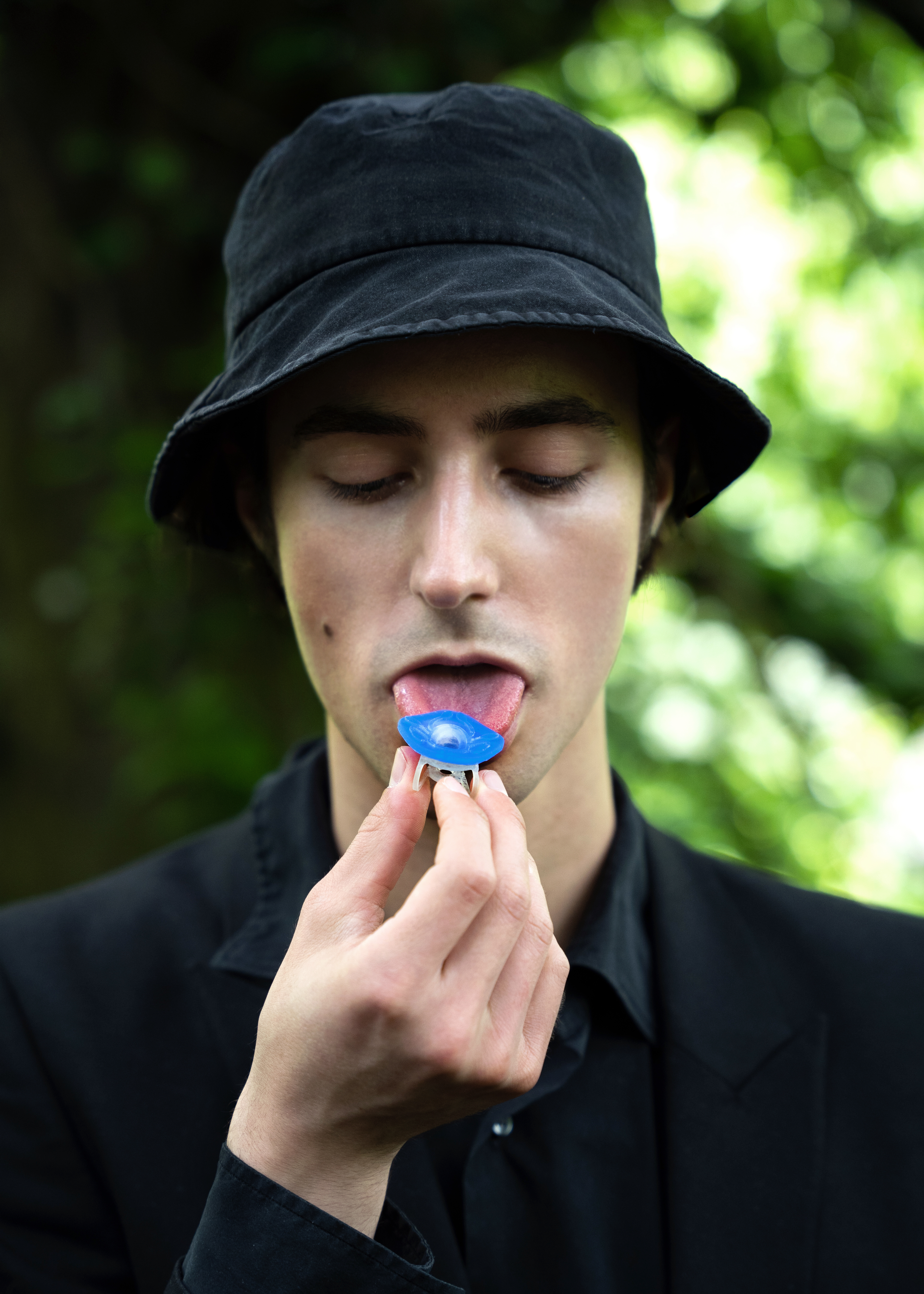 A man in a dark hat touches a blue sensor to his tongue.