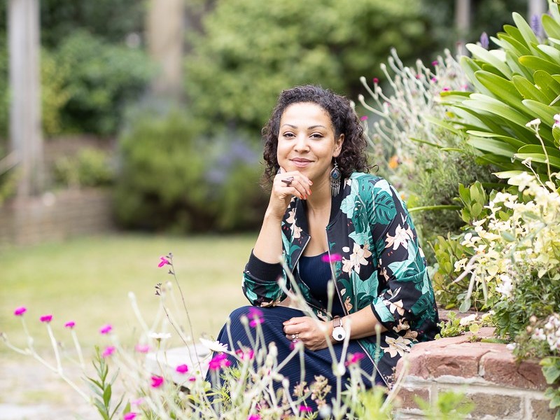 A woman looks to the camera, with flowers in the foreground