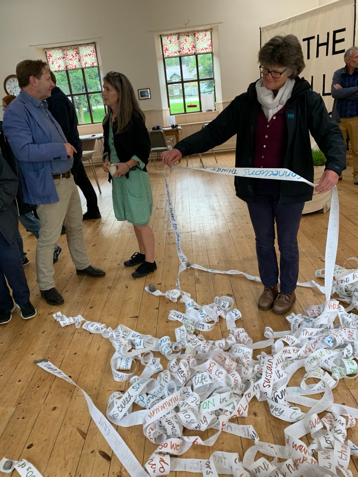 A woman looks through long lines of paper, which have writing on them.