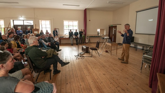 A man stands in front of a seated audience, talking and gesturing as he introduces a film