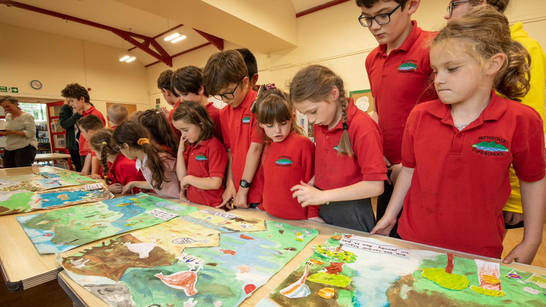 a group of children in red shirts look at hand-painted panels of a story they invented
