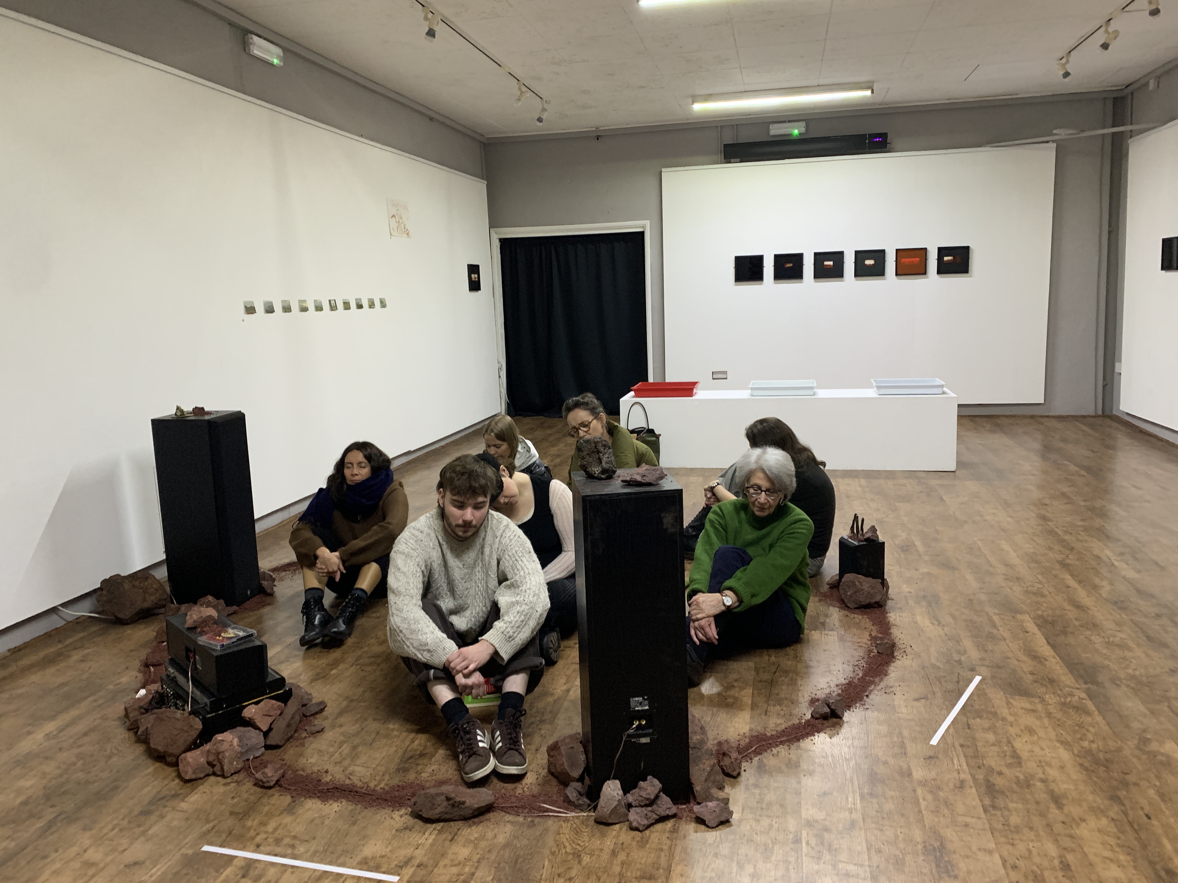 People sit inside a circle with speakers: they are listening to an immersive sound piece, in a gallery