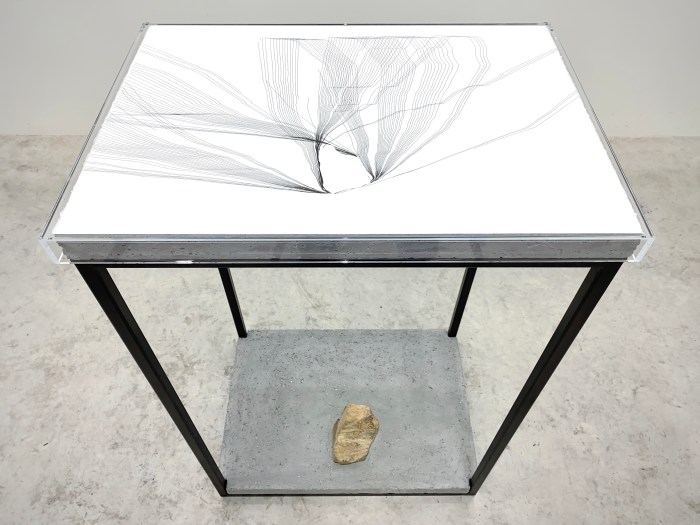 A black and white line drawing on a table, with a stone beneath