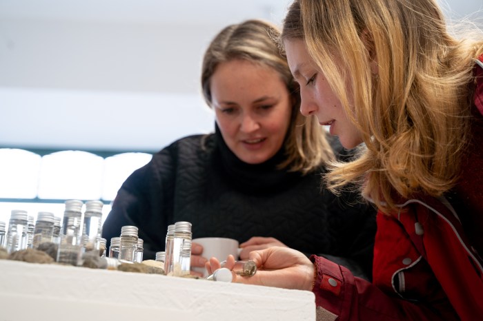 Two women lean over bottles and stones placed on a table