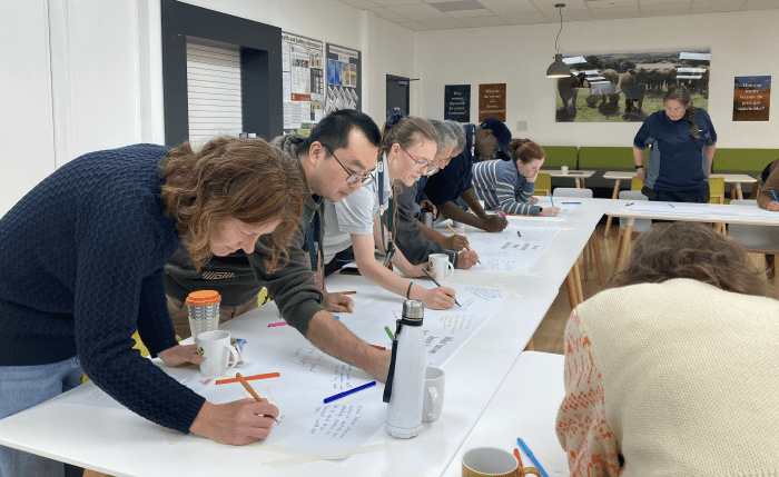 People leaning over a table and writing on a large sheet of paper in a workshop setting