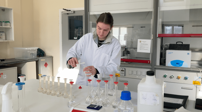 A scientist wearing a white coat and pouring a liquid into a glass container