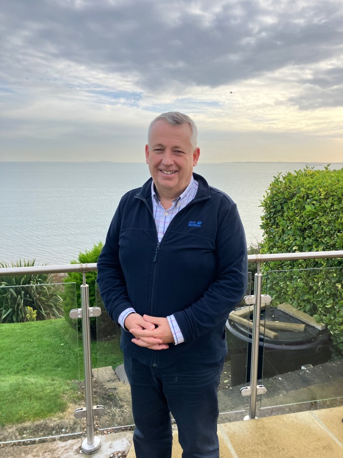 A man standing on a patio with the sea behind him