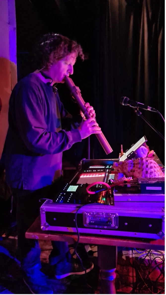 A man plays a wind instrument with pink lighting from a live performance