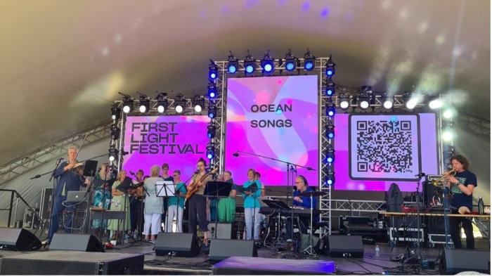 A festival stage with pink screens and a group of musicians and singers