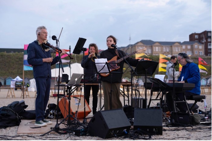 Musicians playing outdoors with music sheets set on stands.