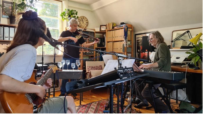 A room with keyboards and three musicians rehearsing