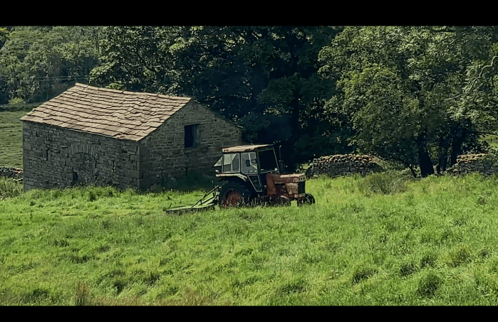 An image of a tractor and a stone built barn, with green grass in a field