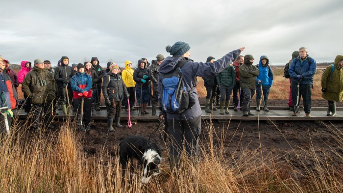A group of people stand on a board walk. One person in the foreground is pointing